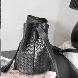 Black handwoven lambskin leather bucket bag with drawstring and shoulder strap on table
