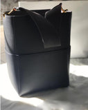 Black genuine leather bucket bag with wide strap and gold hardware on a light surface