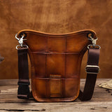 Full grain leather leg bag with stitched details and adjustable brown straps on rustic wood table