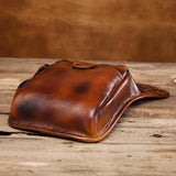 Full grain brown leather leg bag with snap closure on rustic wooden surface
