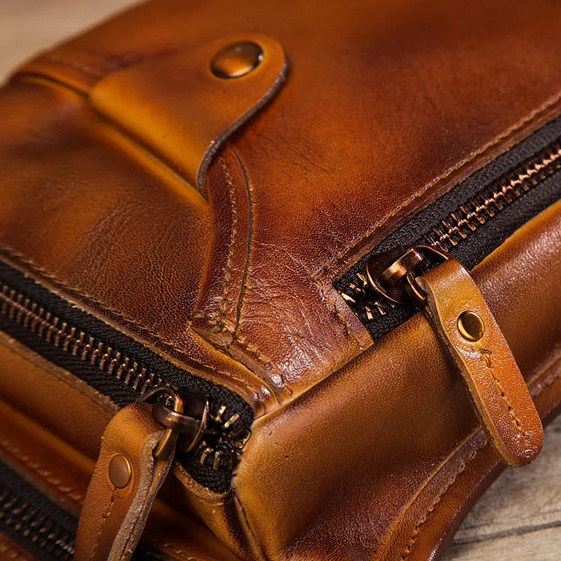 Close-up of a brown full grain leather leg bag with zippers and snap button detail