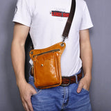 Brown full-grain leather leg bag with zip pocket and adjustable strap worn by man in jeans.
