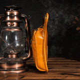 Side view of yellow full grain leather leg bag on wooden table beside vintage lantern