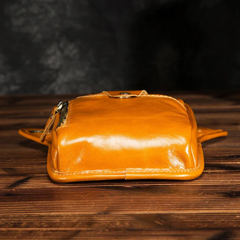 Full grain leather waist bag in tan on wooden surface, zip and button closure visible
