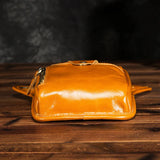 Full grain leather waist bag in tan on wooden surface, zip and button closure visible
