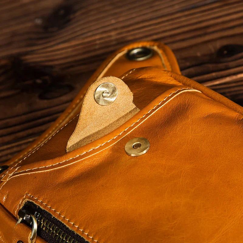Close-up of brown full grain leather leg bag with snap button and zipper on wood surface