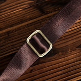 Adjustable brown nylon strap with metal buckle on rustic wood surface, close up