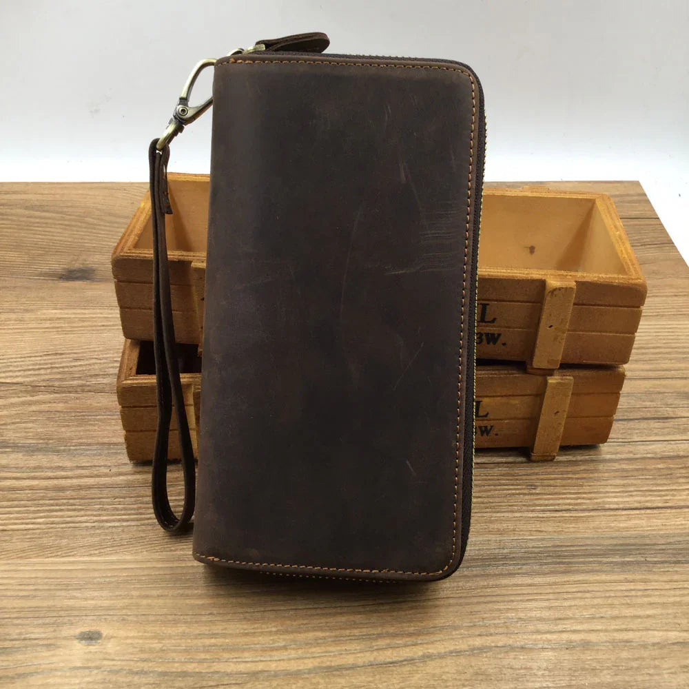Full grain leather long wallet with zipper and wrist strap on wooden surface