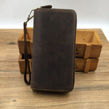 Full grain leather long wallet with zipper and wrist strap on wooden surface