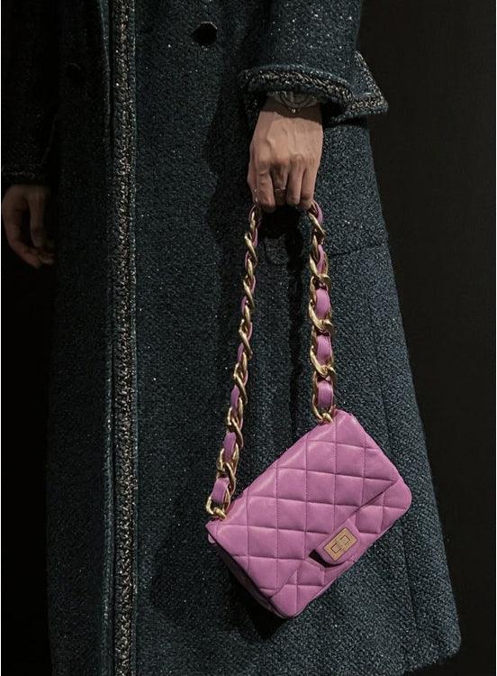 Purple quilted leather shoulder bag with gold chain strap held by person in dark coat