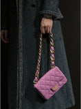 Purple quilted leather shoulder bag with gold chain strap held by person in dark coat