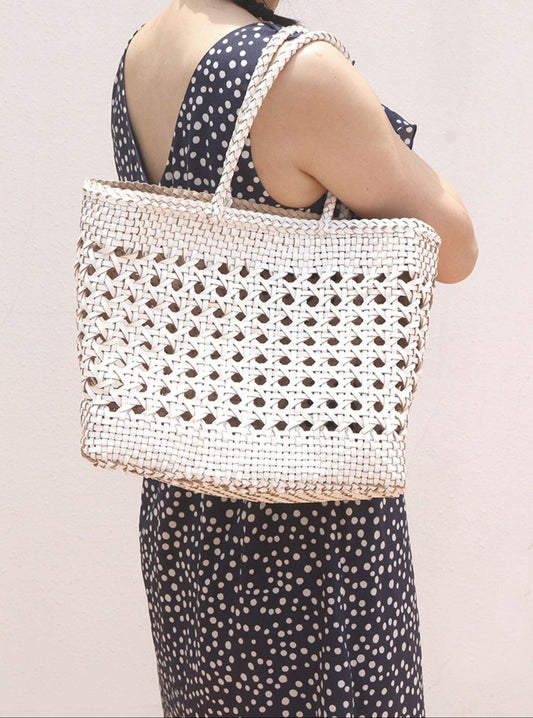 Woman carrying a hand-woven genuine leather tote bag with cuboid shape and open rattan weave