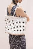 Woman carrying a hand-woven genuine leather tote bag with cuboid shape and open rattan weave
