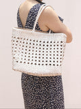 Woman carrying a hand-woven genuine leather tote bag with cuboid shape and open rattan weave