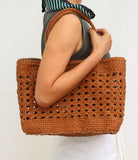 Woman holding a hand-woven genuine leather tote bag with a cuboid shape and braided handles