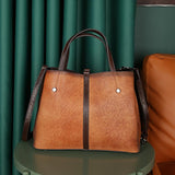 Brown genuine leather tote bag with dark handles and shoulder strap on green table