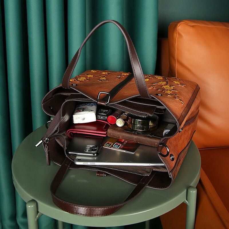 Open brown cowhide leather floral tote bag on table, showing organized contents inside