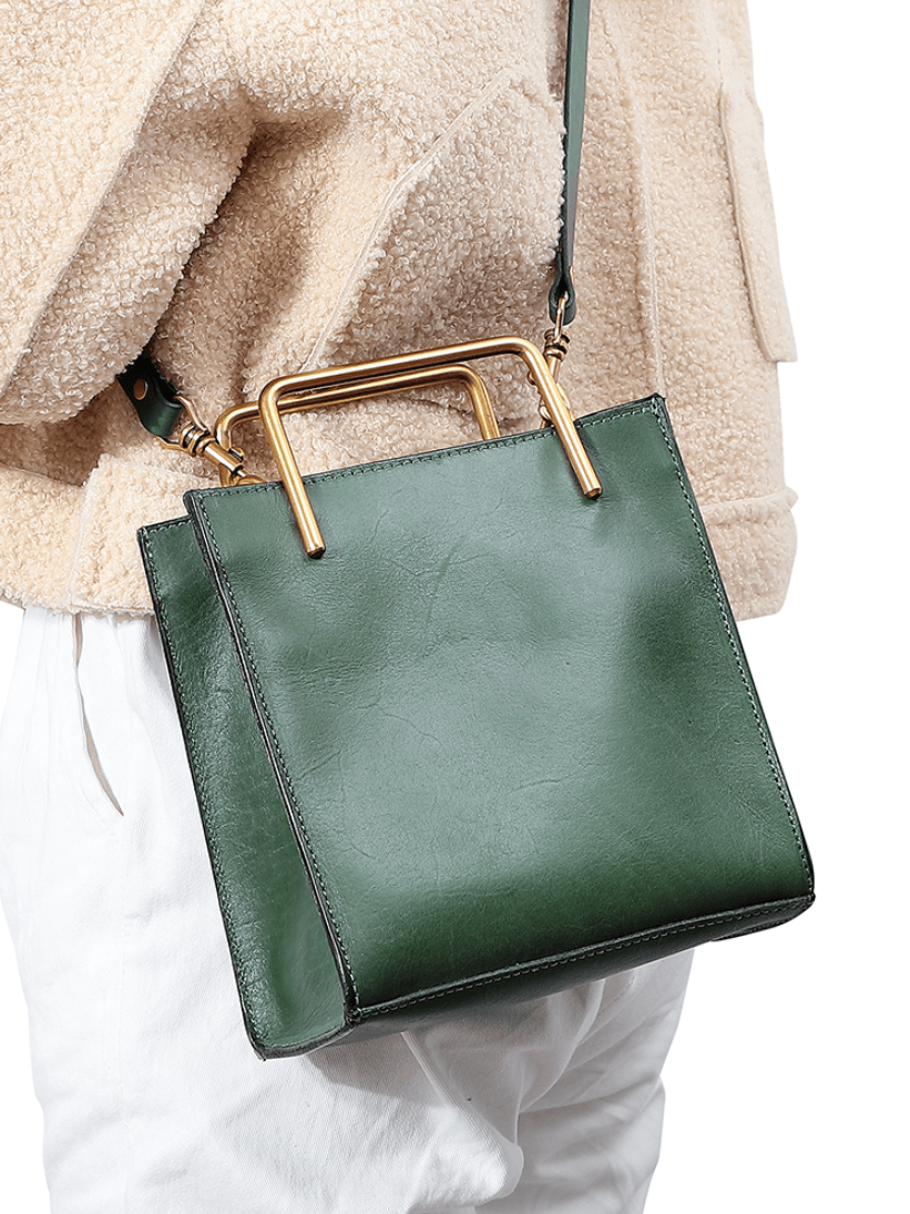Green leather shoulder bag with gold handle and strap, worn crossbody by a woman