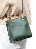 Green leather shoulder bag with gold handle and strap, worn crossbody by a woman