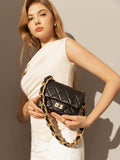 Woman holding a black quilted leather shoulder bag with gold chain strap and turn-lock clasp