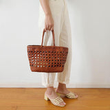 Woman holding a brown handwoven leather tote bag with bamboo-style handles