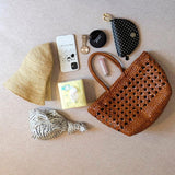 Genuine leather handwoven tote bag with open rattan weave, surrounded by daily essentials.