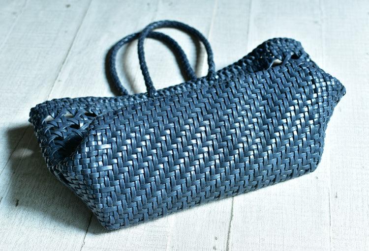 Navy blue handwoven genuine leather tote bag with braided handles on a light wooden surface