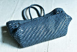 Navy blue handwoven genuine leather tote bag with braided handles on a light wooden surface