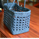 Blue genuine leather hand-woven cuboid tote bag with open rattan pattern on wood table