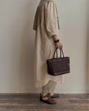 Woman holding a brown handwoven leather tote bag, wearing neutral dress and brown shoes