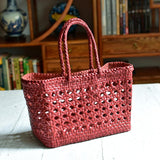 Red genuine leather handwoven tote bag with cuboid shape and woven handles on a table