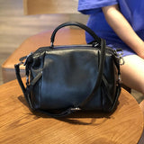 Genuine black leather Boston handbag with top handle and shoulder strap on wooden table