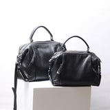 Two black genuine leather Boston handbags with top handles and detachable straps on white display