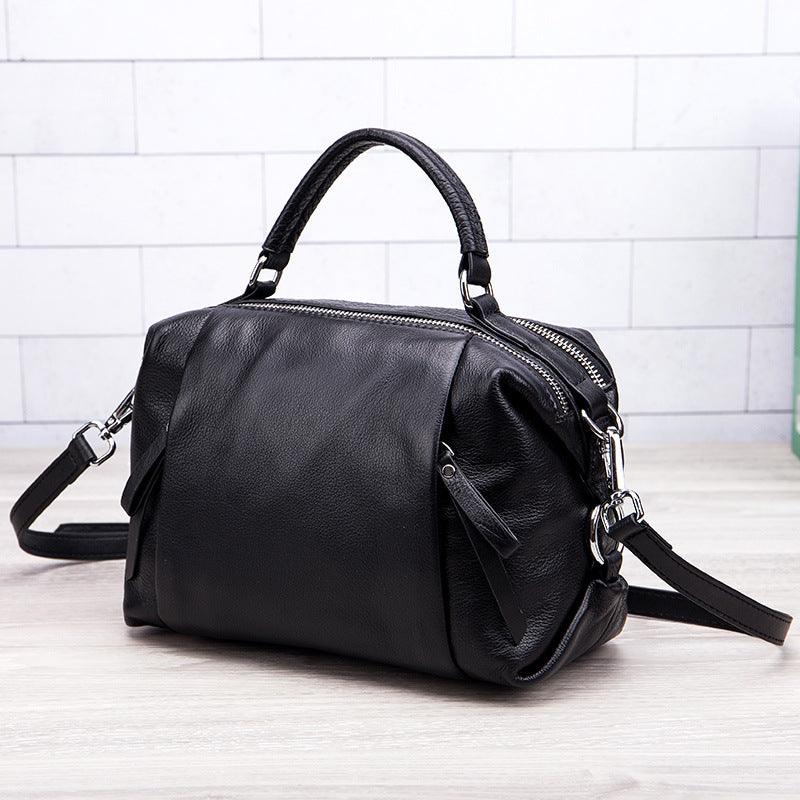 Black genuine leather handbag with top handle and detachable shoulder strap on light background