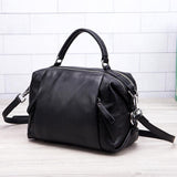 Black genuine leather handbag with top handle and detachable shoulder strap on light background