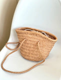 Hand-woven cowhide leather bucket bag with braided drawstring on a white chair