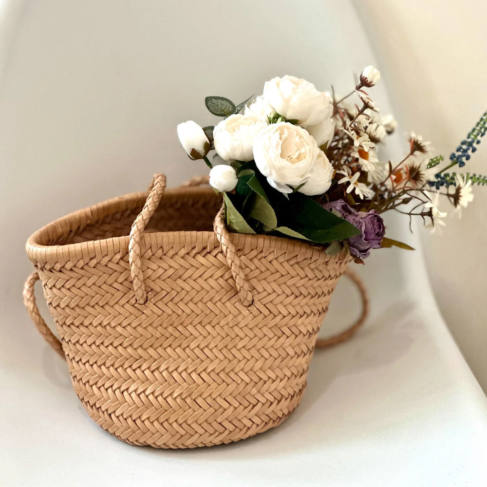 Hand-woven leather bucket bag with braided handles, filled with white flowers