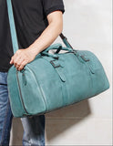 Teal full grain leather duffle bag with shoulder strap, carried by person in casual outfit