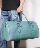 Hand holding teal full grain leather duffle bag with buckles, ideal for travel or gym.