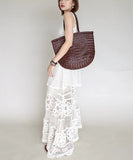 Handcrafted brown woven leather handbag with bamboo-style handles on a neutral background