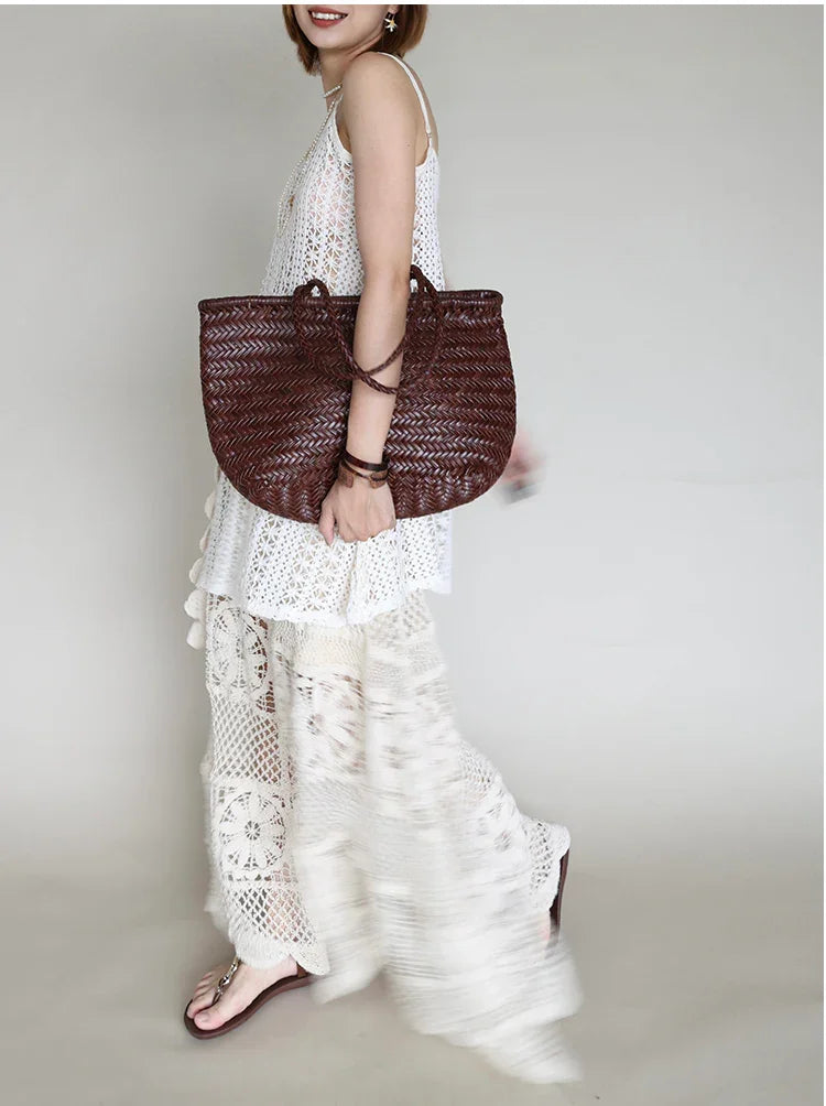 Handcrafted brown woven leather handbag with bamboo-style handles on a neutral background