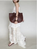 Handcrafted brown woven leather handbag with bamboo-style handles on a neutral background
