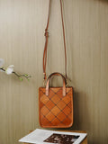 Handcrafted tan cowhide leather handbag with woven diamond pattern, adjustable shoulder strap, displayed against neutral wall.