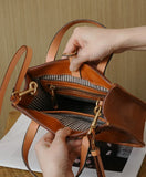 Handcrafted brown cowhide leather handbag with striped interior, zip pocket, and gold hardware