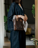 Woman holding a brown handcrafted cowhide leather handbag with tan handles indoors