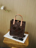 Handcrafted brown cowhide leather handbag with tan handles, quilted pattern, on a wooden stool.