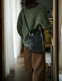 Woman wearing a black quilted leather crossbody bag with top handles indoors