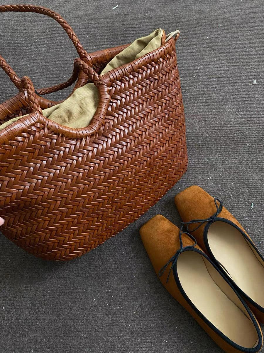 Handcrafted woven leather tote bag with braided handles and a pair of brown suede flats on carpet