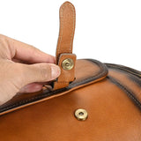 Close-up of a hand fastening a full-grain brown leather duffle bag with a brass snap button
