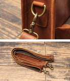 Close-up of brown full grain leather satchel bag straps with brass hardware on wood surface